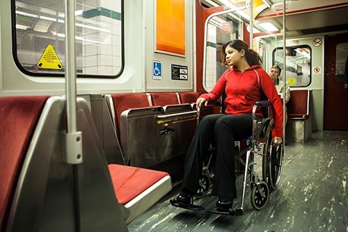 A young woman sits in a wheelchair on a handicapped accessible subway car.